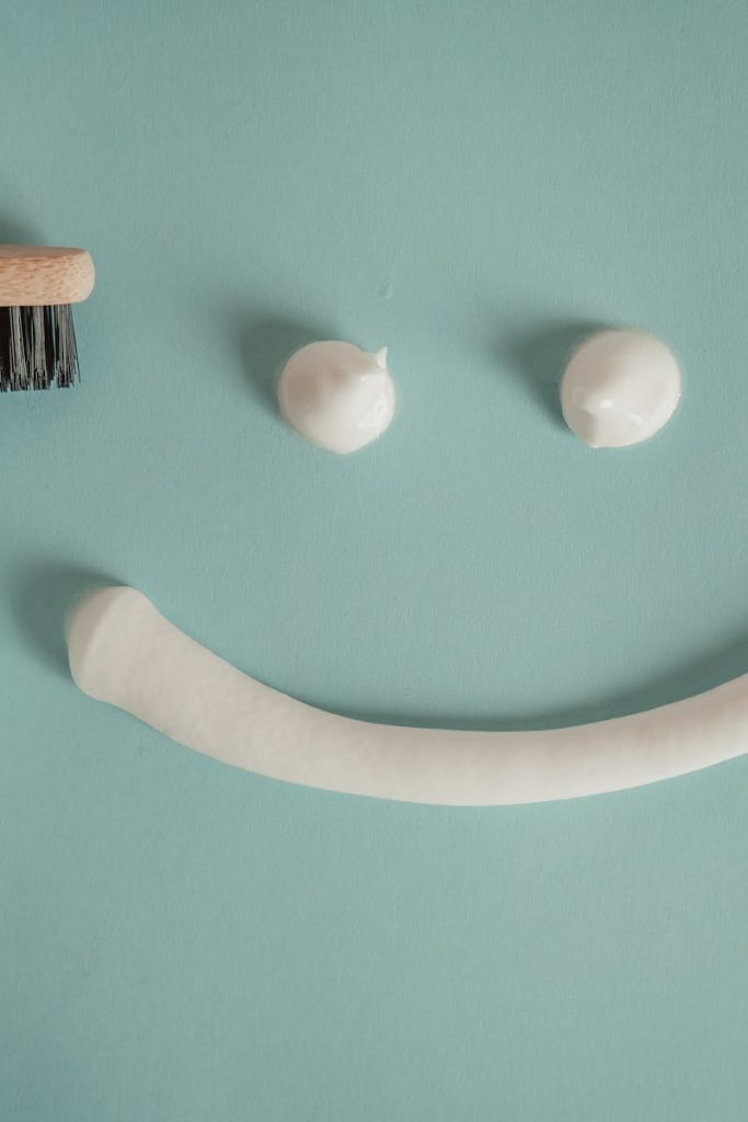 A playful arrangement of toothpaste and toothbrush forming a smile on a blue background.