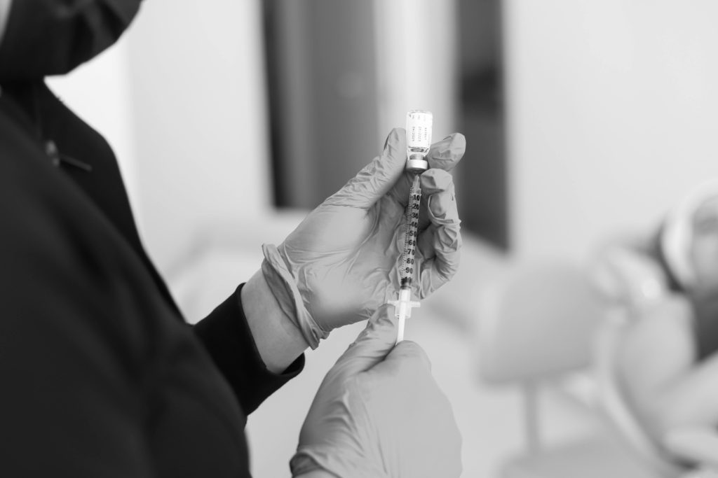 A close-up black and white photo of a medical professional preparing an injection in a clinic setting.